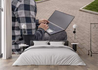 Computer on the lap of a young man in a city park. Leisure of the youth. Wall mural