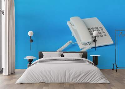 A white telephone with gray buttons on a blue background. Wall mural