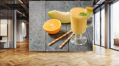 Half an orange, a piece of melon and a mug of smoothie on a wooden table. Wall mural