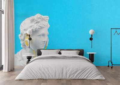 The figure of Apollo with yellow headphones on a blue background. Minimal concept. Wall mural