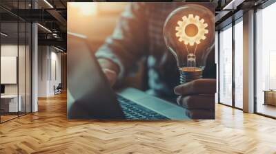 A light bulb with a gear icon represents innovation and creativity in online technology, as a man uses a notebook computer, embodying new ideas and inspiration. Wall mural