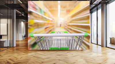 Empty green shopping cart with supermarket aisle with seasoning and cooking vegetable oil bottles product shelves interior defocused blur background Wall mural