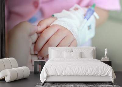 Mother holding child hand with saline IV solution in hospital Wall mural