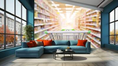 Supermarket aisle product shelves interior blur background with empty shopping cart Wall mural