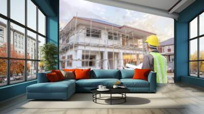 young professional engineer in protective helmet and blueprints paper at the house building construction site Wall mural