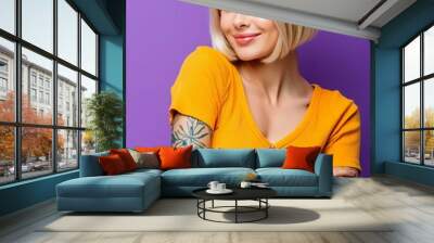 Young blonde woman with arm tattoos isolated on purple background cool edgy vibe yellow shirt Wall mural