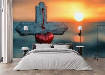 A peaceful scene of a wooden cross with a red heart hanging from it, set against the glowing sunrise over the sea, symbolizing faith. Wall mural