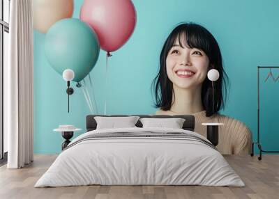 An Asian woman smiling happily, holding a string of three high-floating balloons against a simple background with plenty of space for advertising or promotional content. Wall mural