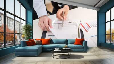 Business man and woman analyzing statistical bar graph and financial reports at desk in the office Wall mural