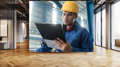 Determined Asian worker writing observations about the manufacturing process indoors Wall mural