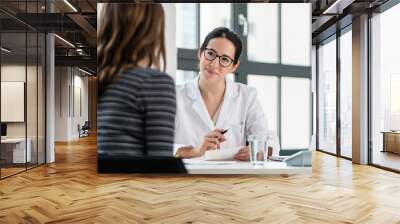 Female physician listening to her patient during consultation while sitting down in the office of a modern medical center Wall mural