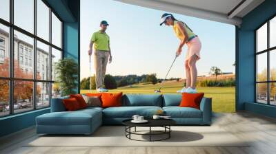 Full length of a woman calculating the trajectory of the ball to the hole, while playing professional golf with her male match partner or instructor outdoors in summer Wall mural