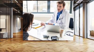 High angle view of a young physician listening to his patient with respect and dedication, during a private consultation in the office of a modern medical center Wall mural