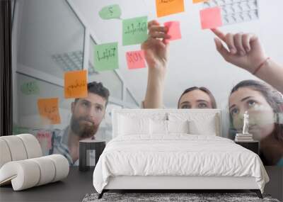 Low-angle view of reliable young workers posting reminders on the transparent wall of an office, next to their colleague in a modern co-working space Wall mural