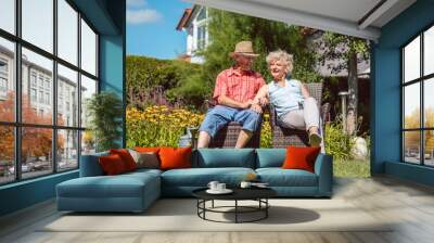 Low-angle view portrait of a happy senior couple in love sitting on chairs, while relaxing together in the garden at home in a sunny day of summer Wall mural