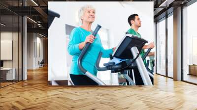 Senior woman on elliptical trainer exercising in gym Wall mural