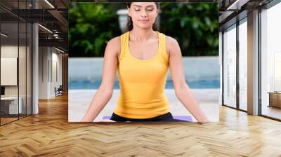 Serene young woman sitting in lotus position while practicing Hindu yoga outdoors Wall mural