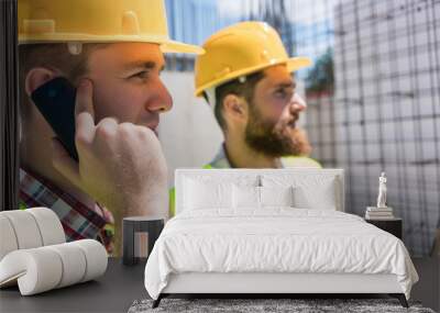 Side view close-up of a worker wearing yellow hard hat while talking on mobile phone during work, on the construction site of a building in progress Wall mural