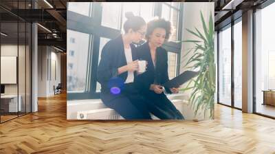 two young female colleagues reviewing business reports during break in the office Wall mural