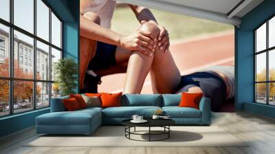 Knee injury, first aid and friend at stadium after running accident or fall. Rehabilitation, physiotherapy and person help athlete on race track with leg pain, muscle or joint inflammation outdoors. Wall mural