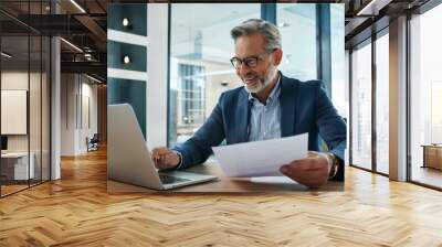 Happy busy older professional businessman entrepreneur using laptop holding bill corporate document in office. 50 years old man executive manager or business owner reading paper working on compute Wall mural