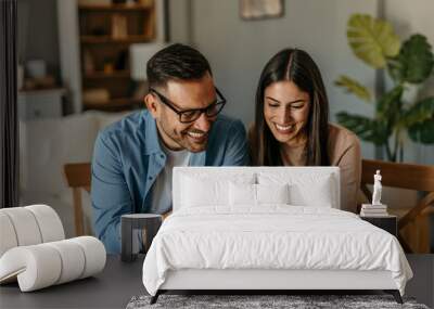 A couple in love is sitting together at a table, using a laptop and a payment card, while both are looking at products on the screen Wall mural