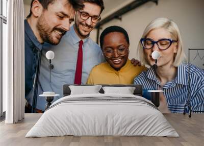 A group of four business professionals, representing various ethnicities, sharing a laugh during a smartphone discussion Wall mural