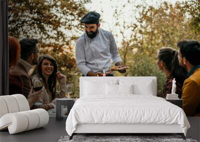 A male chef in uniform is serving a private elegant dinner to a group of people, People are smiling and welcoming the chef who is serving and bringing delicious food. Wall mural