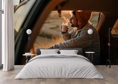 A man sits in the trunk of a car and drinks a fresh hot coffee by himself. Travel alone concept Wall mural