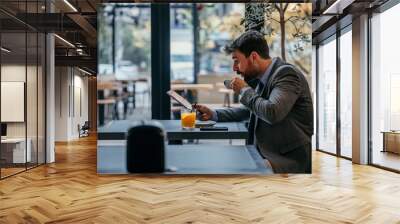 Handsome businessman sitting in the hotel, having a coffee and juice and working on a digital tablet. Copy space Wall mural