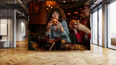 Hungry woman eating a burger while gathering with friends in a pub Wall mural