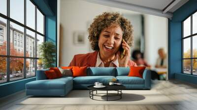 Mature successful businesswoman talking on the phone and working with laptop in a corporate office Wall mural