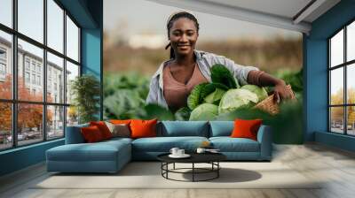 Portrait of a dedicated black woman holding a crate full of fresh cabbage in her hands on the farm outdoors. Wall mural