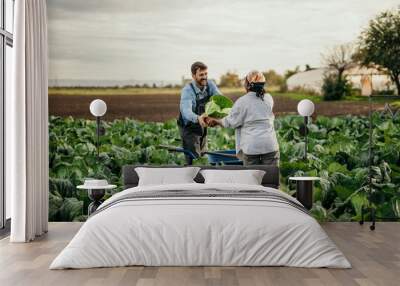 Shot of an attractive young female and male farmers in working clothes carrying a crate of fresh produce. Wall mural