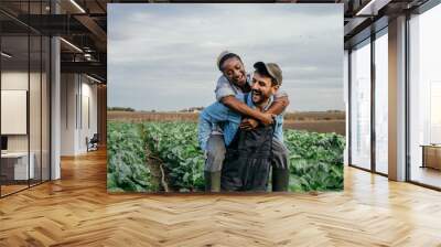 Smiling embraced diverse working couple having a piggyback ride and fun while spending time on their farm together. Wall mural