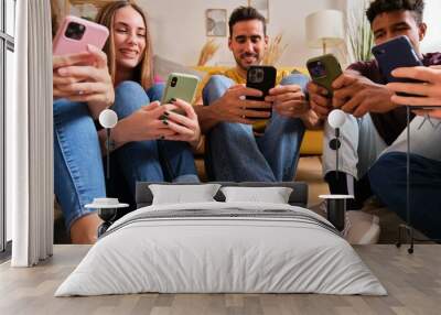 Multiracial friends looking at their mobile phones sitting on a semicircle at a shared students flat. Wall mural