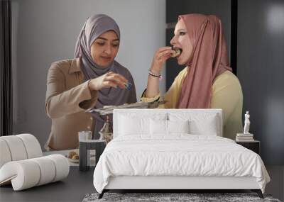 Two young muslim women eating arabic sweets and drinking tea at the kitchen table. Wall mural