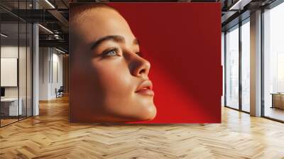 A striking portrait of a person with a shaved head, gazing upwards, bathed in warm light against a vibrant red background, showcasing beauty and serenity. Wall mural