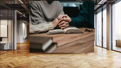 Group of Christians sit together and pray around a wooden table with blurred open Bible pages in their homeroom. Wall mural