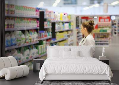 Woman shopping in supermarket reading product information.woman choosing laundry detergent in supermarket Wall mural