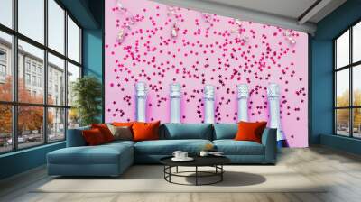 Five Champagne bottles with confetti stars and party streamers on pink background. Copy space,top view. Party background Wall mural