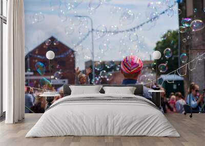 a freelance clown blowing hundreds of tiny, small and big bubbles at outdoor festival in city center Wall mural