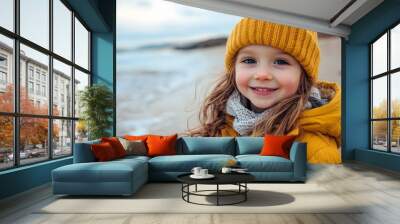 Happy little girl in yellow winter clothes smiling at the beach on a cold day.. Wall mural