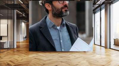 An architect holding blueprints, standing confidently at a construction site Wall mural