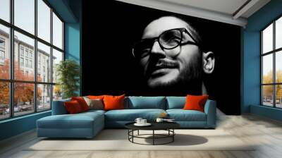 Black and white, close-up dark portrait of young smiling man wearing glasses. Wall mural