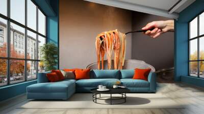 Close-up of female hand holding a spoon with pasta above pot on kitchen stove. Wall mural