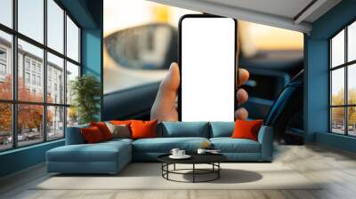 Close-up of male hand holding smartphone with white mockup on screen against blurred background of car interior. Wall mural