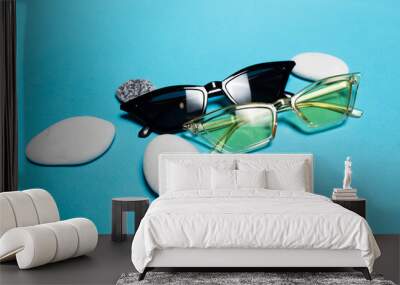 Close-up of modern two sunglasses of yellow and black color near white and grey stones on blue background. Wall mural