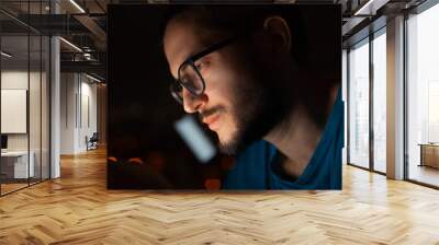 Night portrait of serious man looking in smartphone on background of window. Wall mural