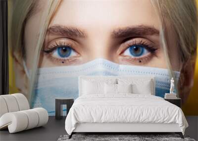 Panoramic portrait, close-up of young girl with blue eyes wearing safety medical flu mask against coronavirus, on yellow color background. Wall mural